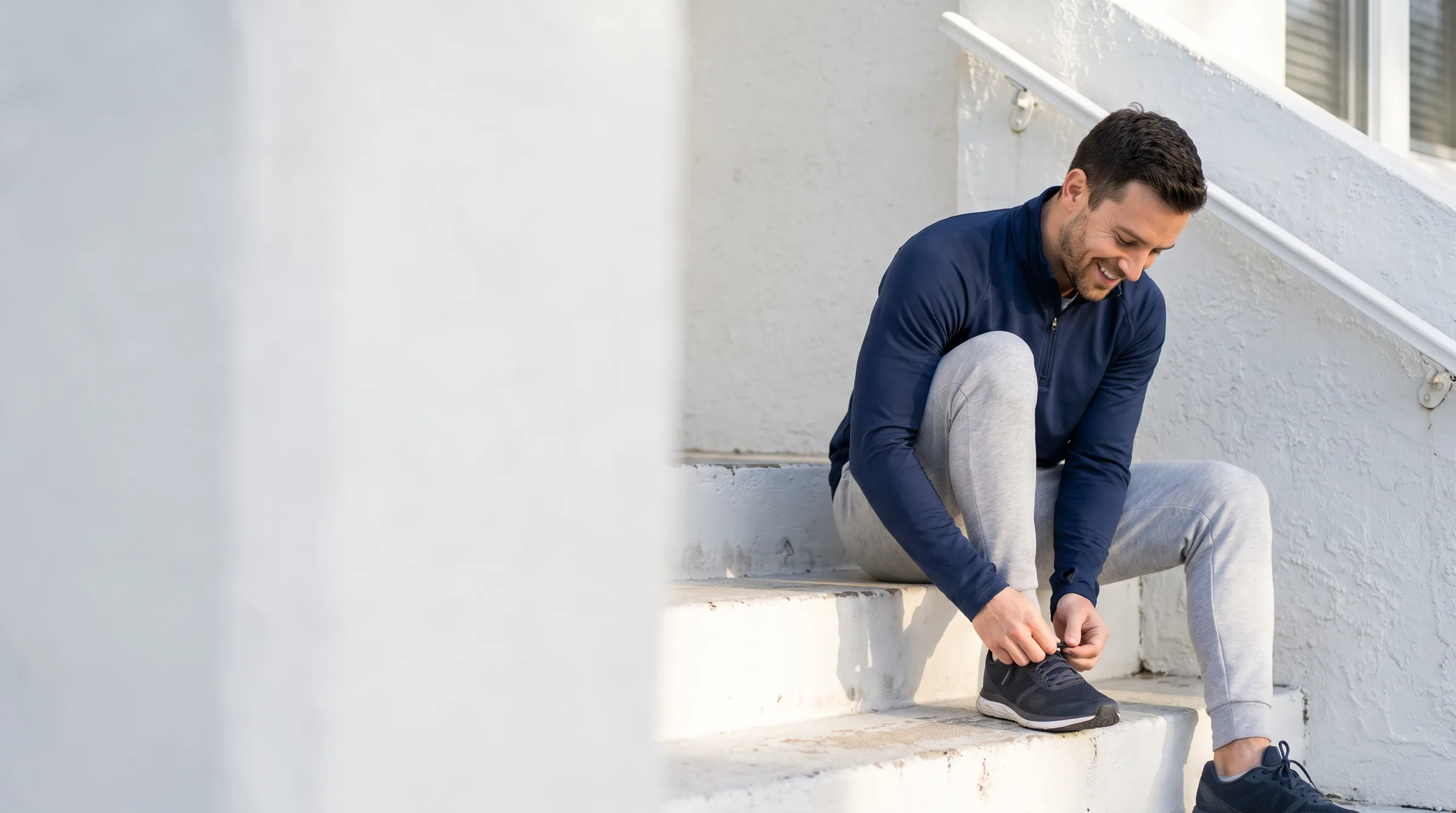 Man smiling while tying his sneakers on the front steps of his home